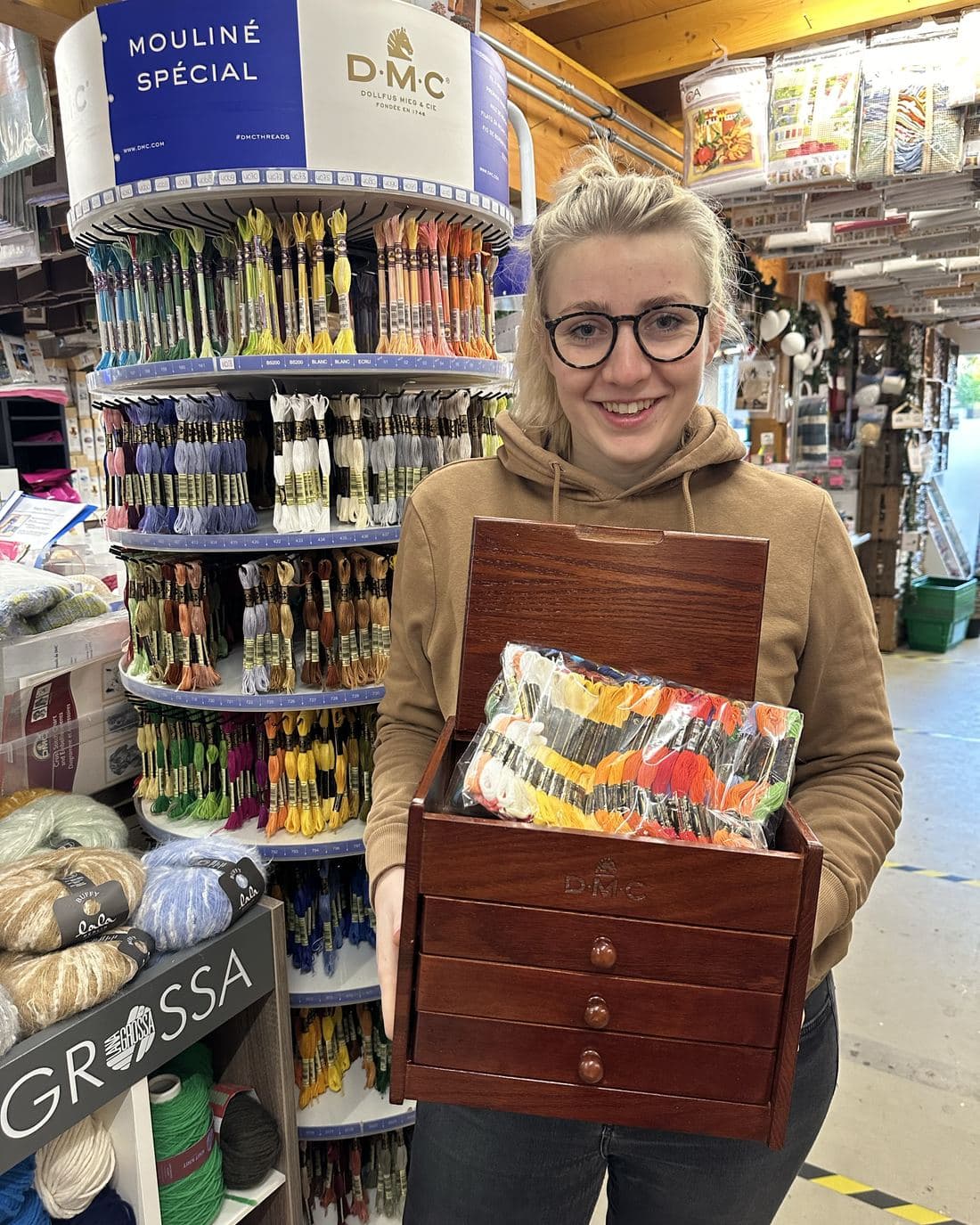 Een medewerker met een houten DMC-ladekast vol borduurgarens, voor de garenmolen.